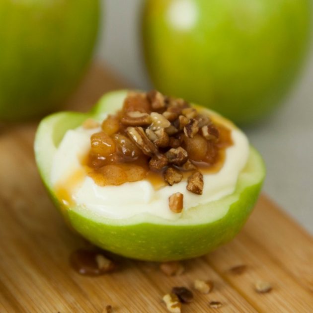 A half apple filled with cheesecake and topped with toasted pecans and caramel sauce