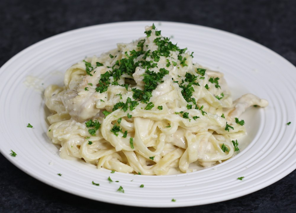 Chicken Alfredo on a serving plate garnished with minced parsley