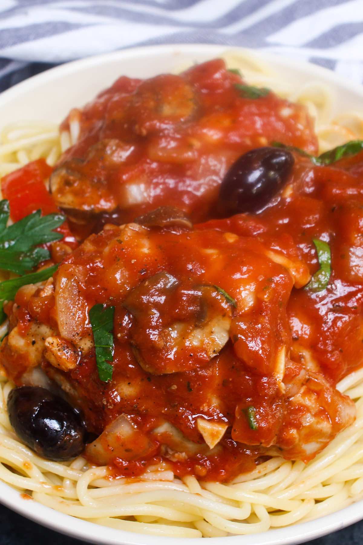 Crock pot chicken cacciatore served on spaghetti pasta on a white plate. 